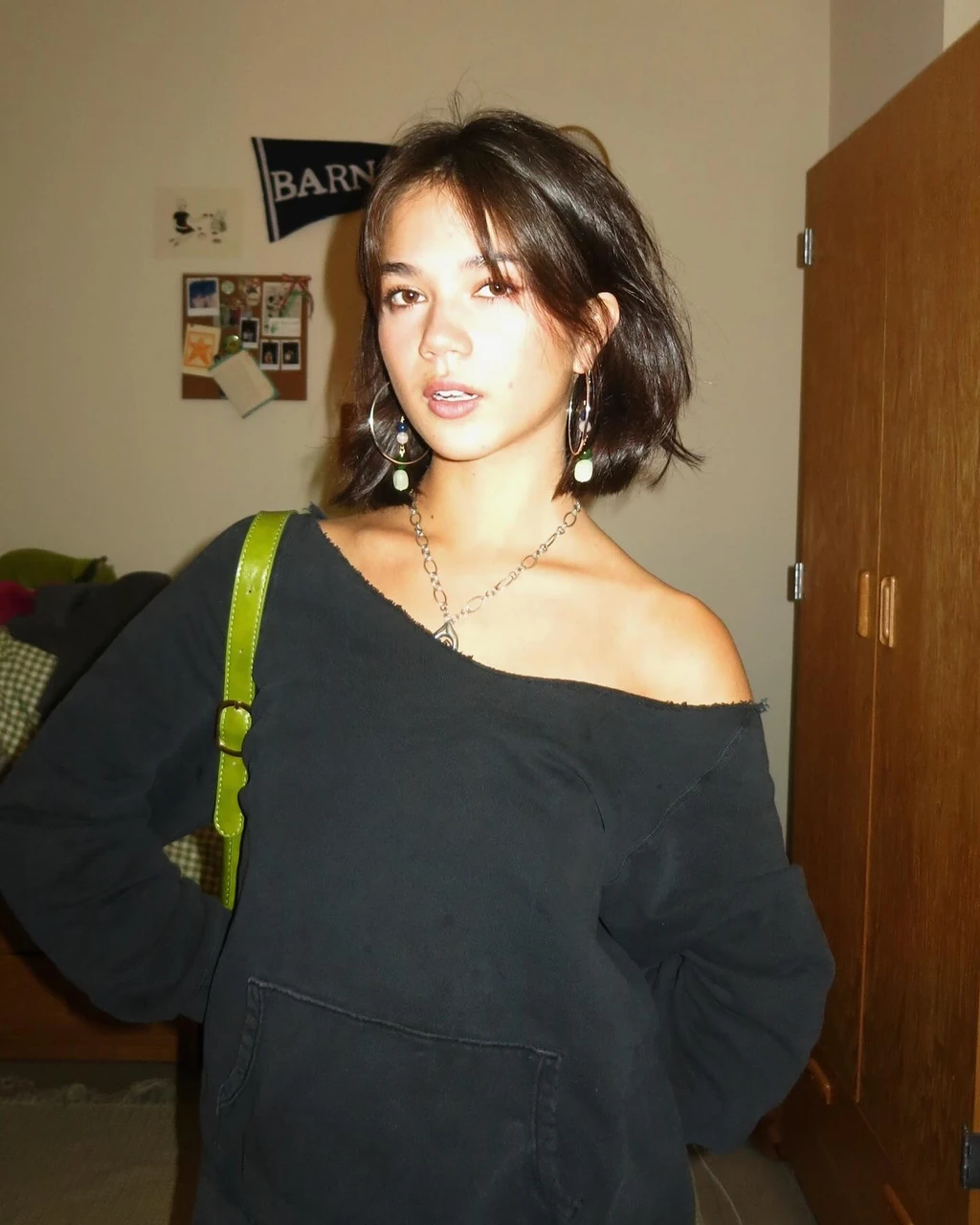 A woman in a black off-shoulder sweater with a green shoulder bag